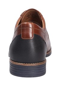 Chaussure en cuir marron avec un talon noir texturé. Présente une forme arrondie, des matériaux contrastants, et un subtil détail de couture le long de la tige.