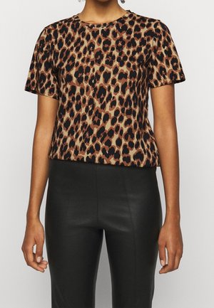 Haut à manches courtes en imprimé léopard dans des tons beige et marron, avec un col rond et une texture douce, associé à un pantalon noir élégant.