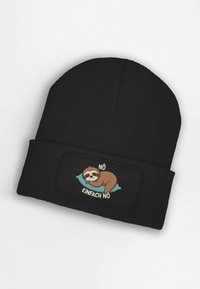 Black beanie hat with ribbed texture, featuring a patch of a sloth on a blue pillow with the text "NÖ" and "EINFACH NÖ."