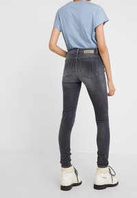 Jeans ajustados grises con una cintura de altura media y cinco bolsillos, combinados con una camiseta de manga corta azul clara y botines blancos. 