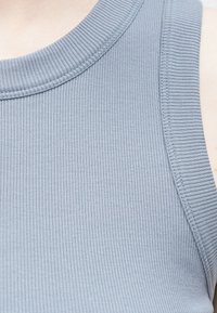 Błękitny prążkowany top na ramiączkach z zaokrąglonym dekoltem i bez rękawów, o gładkiej fakturze materiału i subtelnych detalach szwów.