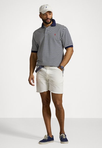 Mørkeblå og hvit stripete polo-skjorte med krage, kombinert med hvite denimshorts, fullført med blå sneakers og en hvit caps.