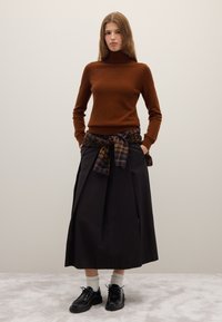 Brown wool turtleneck sweater, black pleated midi skirt, plaid shirt tied at the waist, and black lace-up shoes with white socks.