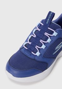 Chaussure de sport bleue avec tige en mesh et synthétique, présentant un design de lacets texturé en bleu clair et lavande, avec une semelle blanche et un accent de logo.
