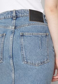 Ljusblå denimjeans med hög midja, med en svart läderetikett på baksidan av midjan och två bakfickor med sömdetaljer.