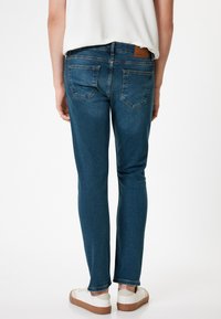 Mörkblå slim-fit jeans med fem fickor, subtila s�ömmar och en läderpatch med varumärke på midjan. Stylade med vita sneakers.