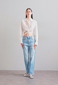 Vit kortärmad skjorta med spetsdetaljer och knyt framtill, ihop med ljusblå raka jeans och silverfärgade lägenheter. Släta texturer och avslappnad passform.