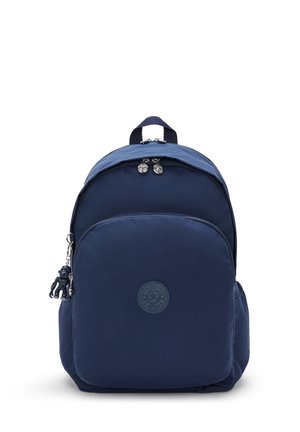 Navy blue nylon backpack with a circular logo, zippered front pocket, top handle, and decorative keychain. Smooth texture, rounded shape.