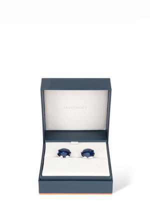 Silberfarbene Manschettenknöpfe mit tiefblauen Glassteinen, präsentiert in einer marineblauen Box, die mit weichem weißen Stoff ausgekleidet ist. Die Box verfügt über einen magnetischen Verschluss.