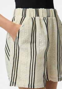 Pantaloni corti a vita alta in tessuto cremoso testurizzato con strisce verticali nere, dotati di tasche laterali e una vestibilità comoda.