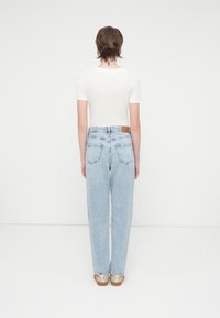 Lys blå høy-levd jeans med rett ben, med baklommer og en brun lærlabel i midjen. En enkel hvit topp med korte ermer.