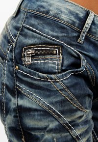 Jeans in denim sbiadito blu con cuciture contrastanti in bianco e giallo, caratterizzati da una piccola tasca con zip sul retro.