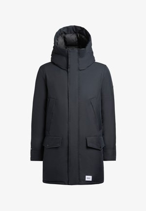 Cappotto lungo blu scuro con colletto alto, cuciture visibili, due tasche frontali e un logo sull'orlo inferiore. Tessuto dalla consistenza morbida.