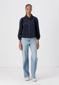 Navy corduroy button-up shirt with a collar, puffed sleeves, and front buttons; paired with light blue straight-leg jeans and white sneakers.