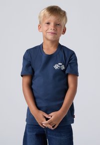 Mørkeblå bomulls t-skjorte med korte ermer, med hvite kryssete rutete flaggdesign på venstre bryst og rund halsåpning.