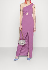 Violetti olkapäältä avattu mekko, jossa on aukko yksityiskohtana ja reiden korkeudelle ulottuva halkio, valmistettu teksturoidusta kankaasta. Yhdistetty pieneen metalliseen käsilaukkuun ja sinisiin korkokenkiin.