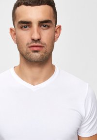 Biela tričko s výstrihom do V a krátkymi rukávmi, vyrobené z hladkej bavlny. Má priliehavý strih a minimalistický dizajn.