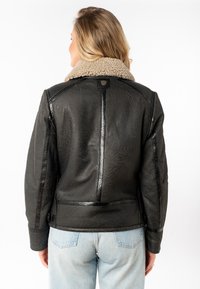 Zwarte leren jas met een gestructureerde afwerking en een beige nepbont kraag. Kenmerken zijn een getailleerde snit en minimale hardware details.