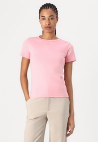 T-shirt rose à manches courtes en tissu doux et lisse. Présente un col rond et une subtile marquage sur la poitrine.
