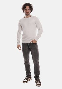 Maglione bianco lavorato a maglia con scollo rotondo, abbinato a jeans slim-fit grigio scuro e sneakers alte marroni con dettagli bianchi.