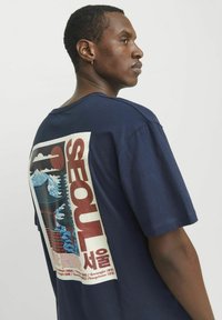 Marine t-shirt med grafisk tryk på ryggen med bjerge, træer og ordet "SEOUL" i fede røde bogstaver. Kortærmet, lavet af bomuld.