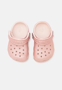 Różowe, brokatowe chodaki z zaokrąglonym noskiem, tylnym paskiem i wieloma otworami wentylacyjnymi. Gładki materiał plastikowy z logo po boku.