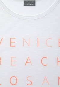 Bílé bavlněné tričko s velkým korálově zbarveným nápisem "VENICE BEACH" v různých tloušťkách a stylech písma. Kulatý výstřih.
