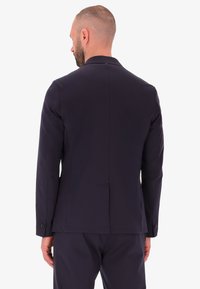 Blazer blu navy con vestibilità su misura, spacchetto singolo sul retro, rever a punta e polsini con bottoni. Tessuto liscio con una sottile texture.