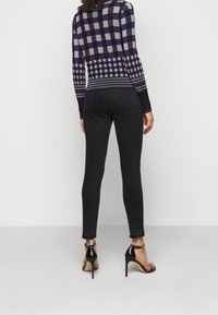 Jean skinny noir avec une texture lisse, associé à un pull violet et gris à motifs. Sandales à talons hauts noires complètent la tenue.