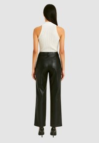 Pantaloni wide-leg in ecopelle nera con tasche frontali, abbinati a un top fitted bianco a coste. Texture liscia, design minimalista.