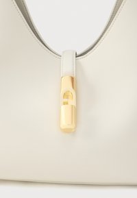 Handtas van roomkleurig leer met een gladde textuur, een gebogen vorm en een gouden slotaccent. Minimalistisch ontwerp met een slank silhouet.