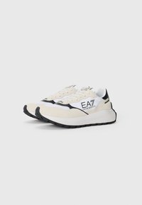 White and cream sneakers with black accents, featuring a suede and synthetic material, curved sole, and a logo on the side.