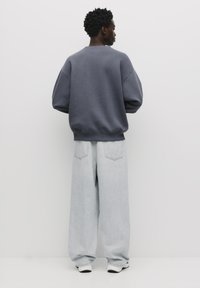 Grå oversized sweatshirt med dropped shoulders, parret med lyseblå baggy jeans. Hvide sneakers er synlige forneden.