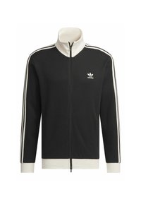 Crna rebrasta jakna sa zipom, bijelim naglascima, visokim ovratnikom i malim bijelim logotipom na lijevoj strani grudi. Ima elastične manžete i rub.