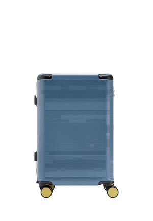 Niebieska walizka z twardą skorupą, poziomymi żeberkami, czarnymi ochronnikami narożników i żółtymi kołami na białym tle.