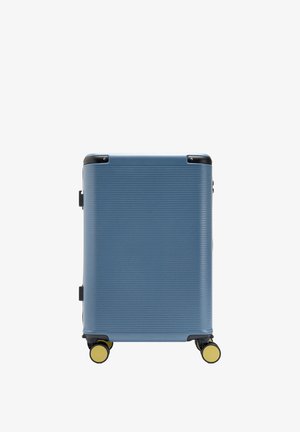 Niebieska walizka z twardą skorupą, poziomymi żeberkami, czarnymi ochronnikami narożników i żółtymi kołami na białym tle.