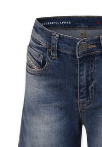 Jeans in denim blu con una trama liscia, cinque tasche, chiusura con bottone e cuciture gialle a contrasto. Etichetta del marchio sulla tasca posteriore.