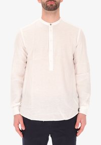 Camicia bianca in lino a maniche lunghe con colletto alla cinese, placca con bottoni e orlo curvato. Il tessuto ha una consistenza leggera e traspirante.