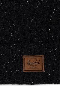 Gorro de punto negro con motas blancas. Presenta un parche de cuero marrón con texto, cosido en la parte frontal. Textura suave, ajuste ceñido.