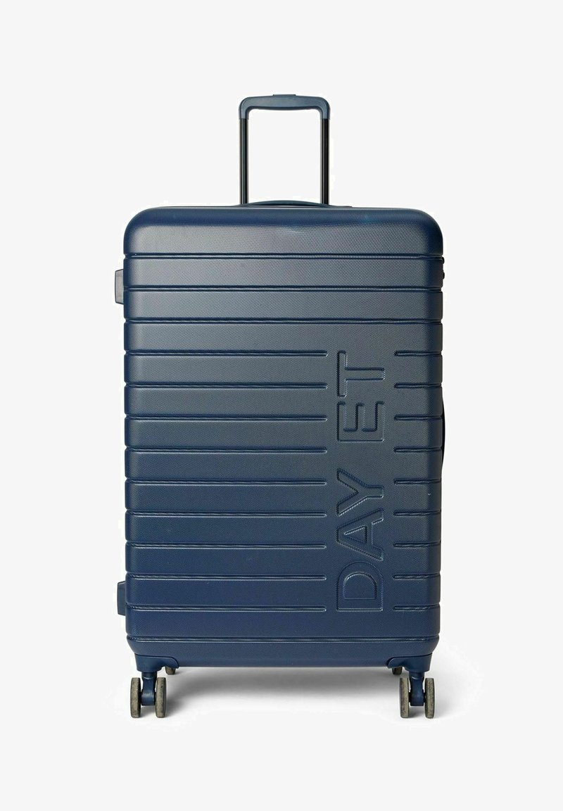 Valise rigide bleu marine avec une texture rainurée verticale, deux roues à roulement fluide, une poignée télescopique et une poignée latérale.