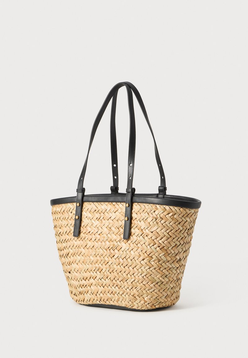 Gewebte Strohtasche mit schwarzen Ledergriffen und Besatz. Sie hat eine runde Form, sichtbare Nähte und Goldakzente.
