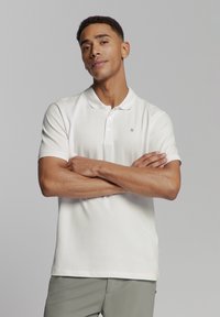 Witte polo shirt van zachte katoen met een drieknopenpoli, korte mouwen en minimale branding op de borst. Soepele textuur, regular fit.