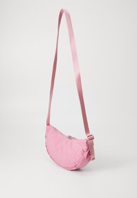 Rosa Stoff-Schultertasche mit einer geschwungenen Form. Verfügt über einen Reißverschlussverschluss und einen passenden verstellbaren Tragegurt. An der gesamten Tasche ist eine glatte Textur.