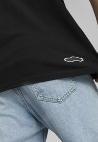Svart bomull t-skjorte med teksturert finish, med en hvit brodert kontur av en bil nær kanten, kombinert med lyseblå denim.