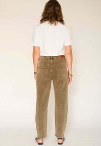 Pantalons ample couleur khaki avec taille haute, cinq poches et écusson en cuir au dos, associés à un t-shirt blanc uni.