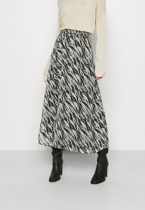 Une jupe maxi à motifs noir et blanc avec un design plissé et une taille élastique, associée à des bottes noires jusqu'aux genoux.