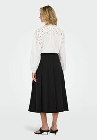 Blusa bianca a maniche lunghe con dettagli a giorno e retro arricciato, abbinata a una gonna nera plissettata e mule nere con tacco.