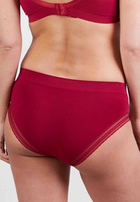 Rode katoenen slip met een gladde afwerking, voorzien van delicate kantaccenten bij de beenopeningen en een brede comfortabele tailleband.