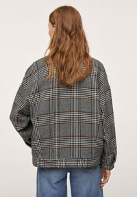 Futrzany oversize'owy płaszcz w szaro-czarną krateczkę z brązowymi akcentami. Posiada miękką teksturę, opadnięte ramiona i luźny krój.