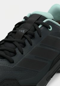 Μαύρο αθλητικό παπούτσι με υφασμάτινο επάνω μέρος, λεπτομέρειες από δίχτυ, ευέλικτο σύστημα κορδονιών και τιρκουάζ πινελιές στον γιακά και τις τρύπες των κορδονιών.